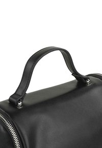 Bolso de cuero negro con una textura suave, que presenta un asa redondeada y detalles de cremallera plateados a lo largo de un lado.