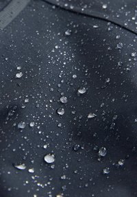 Tejido negro resistente al agua con una textura suave, que presenta numerosas gotas de agua pequeñas y grandes que reflejan la luz.