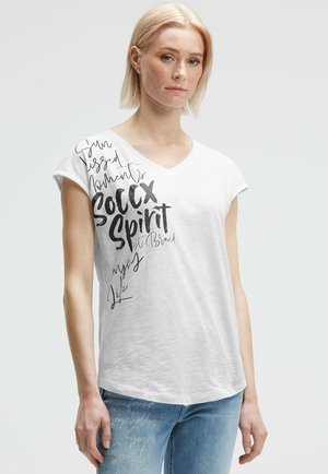 Weißes, kurzärmliges V-Ausschnitt-T-Shirt aus leichtem Stoff, mit schwarzen Schriftzügen und bedrucktem Text auf der Vorderseite, kombiniert mit Jeans.