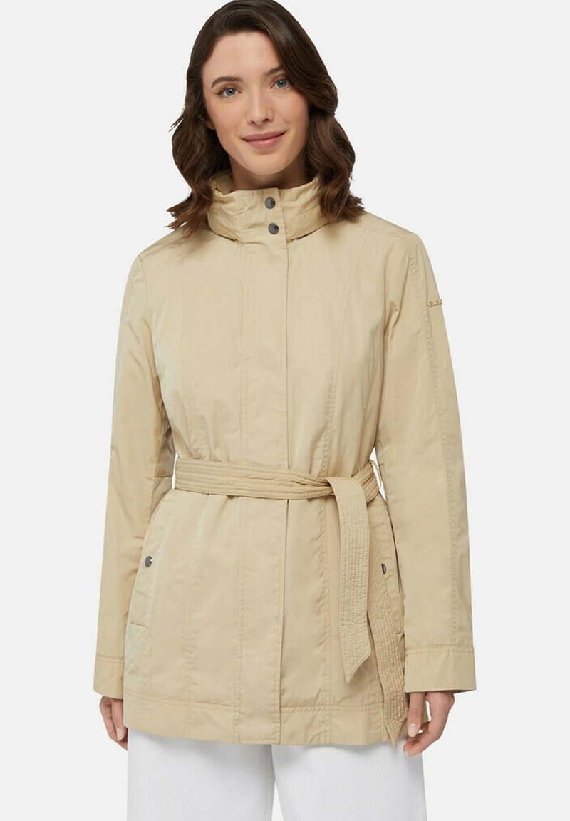 Giacca beige chiaro con cintura, colletto alto, chiusura con bottoni a pressione, tasche laterali e dettagli testurizzati sulle maniche. Tessuto liscio e leggero.