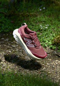 Chaussure de sport en maille rouge avec une semelle beige, arborant un grand logo "N" blanc, des lacets sécurisés et une tige texturée.