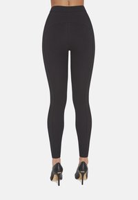 Czarne legginsy o wysokim stanie z kontrastującymi szwami, gładką fakturą i dopasowanym krojem, w zestawieniu z czarnymi szpilkami.