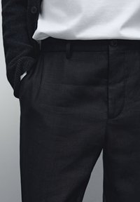 Dark navy linen trousers with a textured surface, featuring a belt loop, front pockets, and a single button closure. Worn with a white shirt.