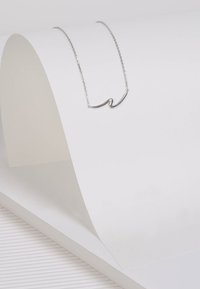 Silberne Kettenhalskette mit einem gewundenen Anhängerdesign. Der Anhänger ist schlank und minimalistisch und liegt auf einer strukturierten weißen Oberfläche.