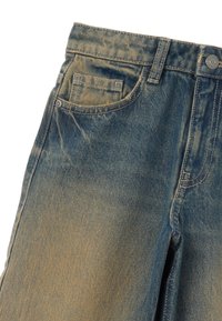 Jean en denim bleu avec une texture délavée, comportant cinq poches, une fermeture à bouton et des détails de couture subtils.