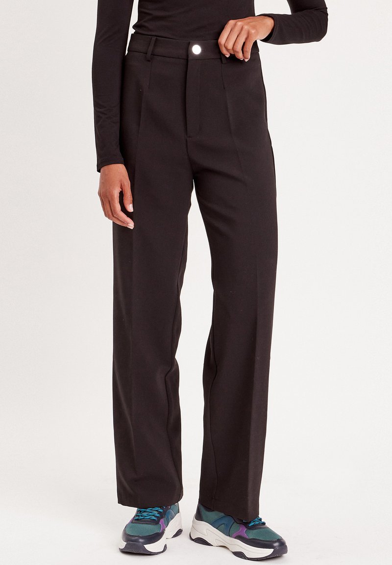 Pantaloni neri a gamba larga con una vita alta, pieghe frontali e un dettaglio lucido sui bottoni. Il tessuto ha una texture liscia e un design sartoriale.