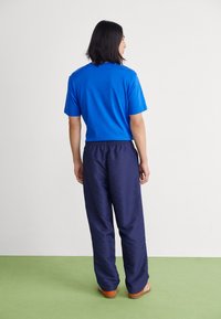 Blå bomulds t-shirt med korte ærmer, parret med navy mønstrede bukser med elastisk talje og orange stribede sandaler.