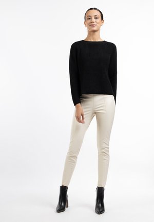Pulover negru tricotat cu dungi, cu mâneci lungi și o croială ușor scurtă, asortat cu pantaloni bej ajustați și cizme negre până la gleznă.