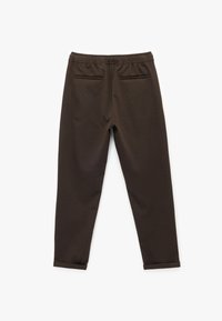 Pantalon de survêtement marron avec une coupe slim, une taille élastique et deux poches arrière ; le tissu présente une texture lisse et un design simple.