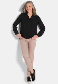 Schwarzes Langarmhemd mit Kragen, kombiniert mit hellbeigen Hosen und schwarzen Sneakers, mit einem lockeren Schnitt und umgeschlagenen Ärmeln.