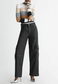 Pantaloni cargo neri con tasche laterali, design a gamba larga e vita alta, abbinati a un dolcevita a righe in cotone e tacchi in argento.