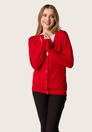 Red cardigan with a V-neck and heart-shaped buttons. Long sleeves, ribbed hem, and soft knit texture. Worn open over a white shirt.
