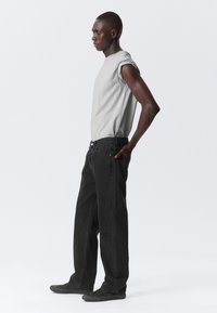 Light gray sleeveless t-shirt paired with loose-fitting, dark gray jeans. The outfit features a casual design and textured fabric.