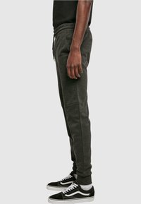 Grijze sweatpants met een trekkoord in de taille en zijzakken, gecombineerd met zwarte sneakers met witte accenten en veters.