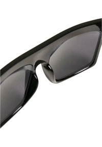Occhiali da sole neri con montatura in plastica elegante e lenti grigie scure. Design angolare con bordi lisci; nessun logo o motivo visibile.