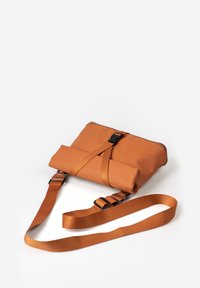 Braune Lederhandtasche mit verstellbarem Riemen und schwarzem Zubehör. Sie verfügt über ein gefaltetes Design und einen Schnallenverschluss, der eine glatte Textur zur Geltung bringt.