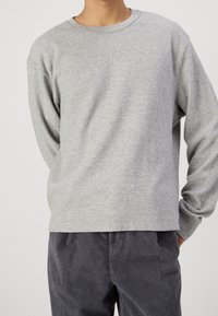 Grijze geribbelde langekoker met ronde hals, met een ontspannen pasvorm en textuurstof; gecombineerd met donkere corduroy broek.
