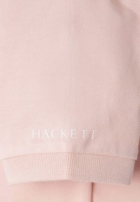 Světle růžové polo tričko z bavlny s texturovanou tkaninou a žebrovanými manžetami. Značka "HACKETT" je vyobrazena bílým písmem na lemu.