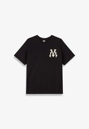 Camiseta negra de algodón, con mangas cortas y cuello redondo. El diseño notable incluye una letra "M" de color crema en el pecho.