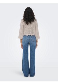 Maglione beige lavorato a maglia con un motivo a coste e maniche a tre quarti, abbinato a jeans blu a vita alta e gamba larga.