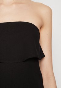 Haut noir sans bretelles présentant un design à volants superposés. Fabriqué dans un tissu texturé avec une finition lisse, mettant en valeur des lignes épurées et une élégance simple.