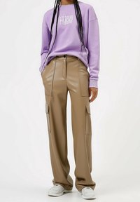 Sudadera lila con el logo "HUGO", combinada con pantalones cargo de cintura alta en beige que tienen bolsillos laterales y una textura suave y brillante. Zapatillas blancas.