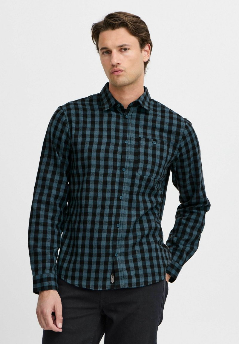 Camicia flanella a quadri nera e teal, con colletto button-down, taschino sul petto e maniche lunghe. Texture morbida, design casual.