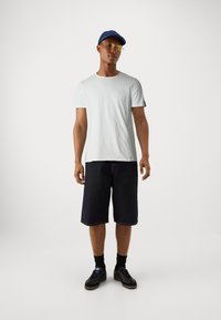 Hvid bomulds t-shirt, mørke denim shorts, sorte sneakers, iført en blå kasket og gule solbriller. Simpelt design, afslappet pasform.