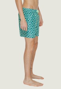 Costumi da bagno turchesi con un motivo ondulato bianco, vita con cordino e tessuto leggero. Progettati per comfort e mobilità.