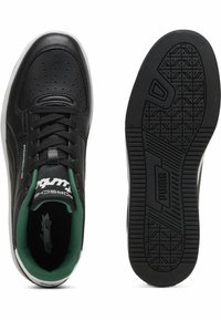Black leather sneakers with perforated design, green mesh interior, white midsole, and textured black rubber outsole. Puma branding visible.