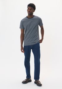 Juostuota pilka ir tamsiai mėlyna trumpomis rankovėmis marškinėliai su apvalia iškirpte, derinami su tamsiai mėlynomis tiesiomis kelnėmis ir tamsiais batais. Paprastas dizainas.