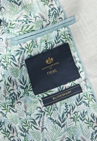 Tissu bleu clair avec un motif floral présentant des feuilles vertes et des accents roses. Comprend une étiquette sombre avec du texte doré et un hashtag.