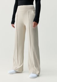 Beige, magas derekú nadrág széles l�ábakkal, sima anyaggal, függőleges varrással, fehér sportcipővel párosítva.