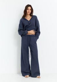 Navyblaues Lounge-Set mit einer knopfbaren Oberseite mit V-Ausschnitt und weit geschnittenen Hosen. Hergestellt aus einem strukturierten Stoff mit lockerer Passform.