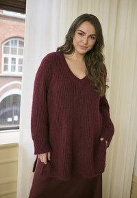 Maglione lavorato a maglia bordò con scollo a V, maniche lunghe e tasche laterali, caratterizzato da un motivo testurizzato e una vestibilità morbida.