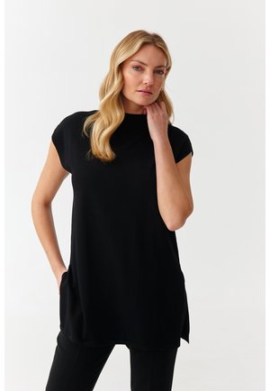 Black tunic with a high neckline, short cap sleeves, and side slits; crafted from smooth fabric, features a relaxed fit and front pockets.