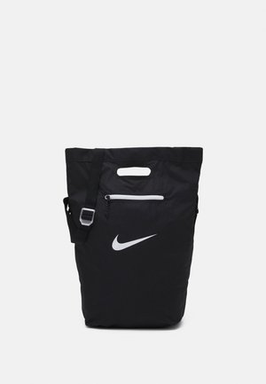 Czarna torba na ramię Nike z białym logo, wycięciem na górne uchwyty, przednią kieszenią na zamek oraz regulowanym paskiem na ramię.
