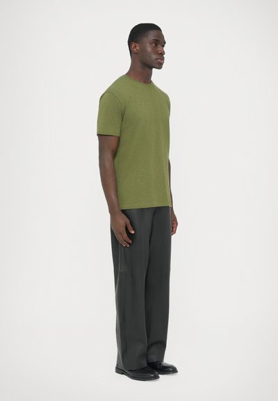Μακό μπλουζάκι σε ελιά πράσινο με κοντά μανίκια, συνδυασμένο με άνετο, χαλαρό σκούρο γκρι παντελόνι και μαύρα παπούτσια. Απλός σχεδιασμός, λεία υφή.