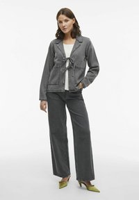 Šedá džínsová bunda s viazaním vpredu, s výstrihom do tvaru V a dvoma prednými vreckami. Vytvorené s širokými šedými džínami a zelenými lodičkami s špicatou špičkou.