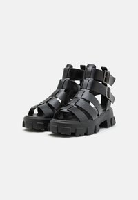Must-haved mustre strappy sandaalid, millel on mati sünteetilise materjali konstruktsioon, avatud varvaste disain, paks tald ja reguleeritavad metallist pandlad.
