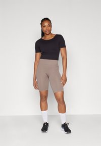 Black cropped t-shirt paired with ribbed, high-waisted brown bike shorts. Model wears black sneakers and white crew socks. Simple, modern fit.