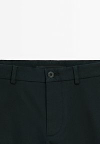 Czarne spodnie z teksturowanej tkaniny, z zapięciem na guzik, szlufkami na pasek i ukośnymi przednimi kieszeniami, widoczne od pasa w górę.