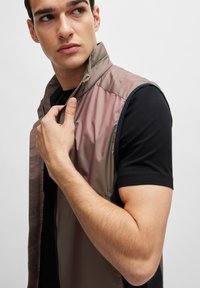Chaleco sin mangas en un degradado de rosa suave y gris, hecho de un material liso y ligero, con un cuello alto y cremalleras.