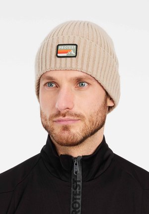 Beige knitted beanie with ribbed texture, featuring a rectangular black and green patch displaying mountains and the word "PROTEST."