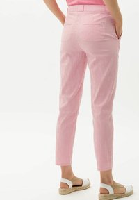 Person i rosa och vita vertikalt randiga byxor med händerna i fickorna och vita espadrillosandaler som står på sidan.