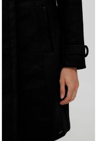 Giacca nera di lana con una tasca con zip, texture morbida e dettaglio sui polsini con un anello. Accento in metallo nella parte inferiore.