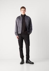 Grå bomberjakke, svart zip-up topp, svarte bukser og svarte chelsea-støvler. Glatt stoff, ribbede mansjetter, tettsittende silhuett, minimalistisk design.