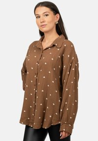 Brown button-up shirt made of textured fabric with a grid pattern, featuring small white heart-shaped accents throughout.