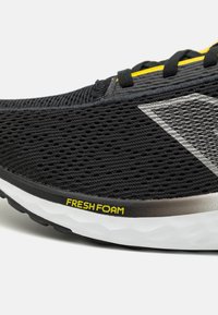 Zapatilla de running negra con parte superior de malla, acentos plateados, una destacada etiqueta "FRESH FOAM" y una suela texturizada para amortiguación.