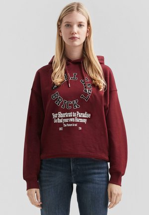 Sweat-shirt à capuche bourgogne avec texte graphique blanc, coupe ample et capuche à cordon. Présente des poignets et un ourlet côtelés, avec une texture douce.